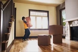 Person carrying moving boxes into an empty living room