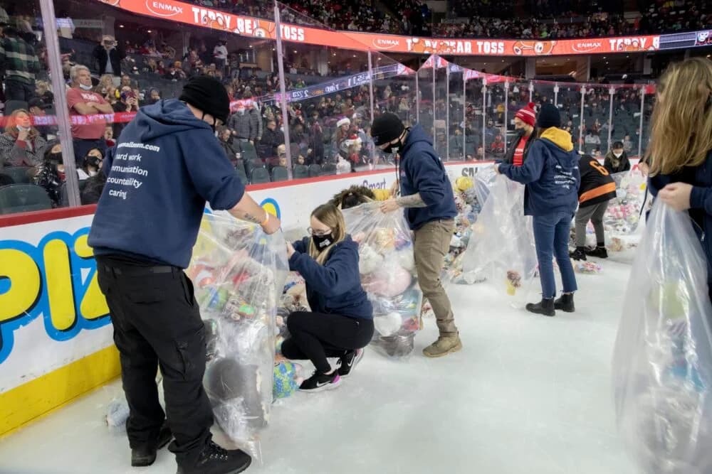 Volunteers collecting teddy bears on the ice during a hockey game.