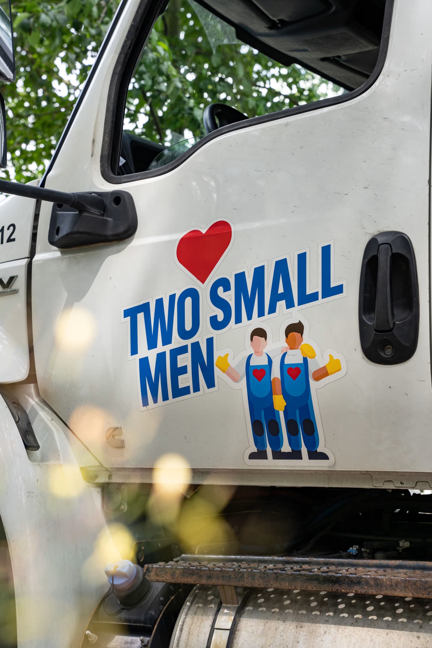 A close-up of a "Two Small Men" moving truck door with the company logo, featuring two cartoon movers and a red heart, visible on the side.
