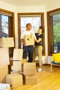 Couple standing in a room with moving boxes, smiling at each other