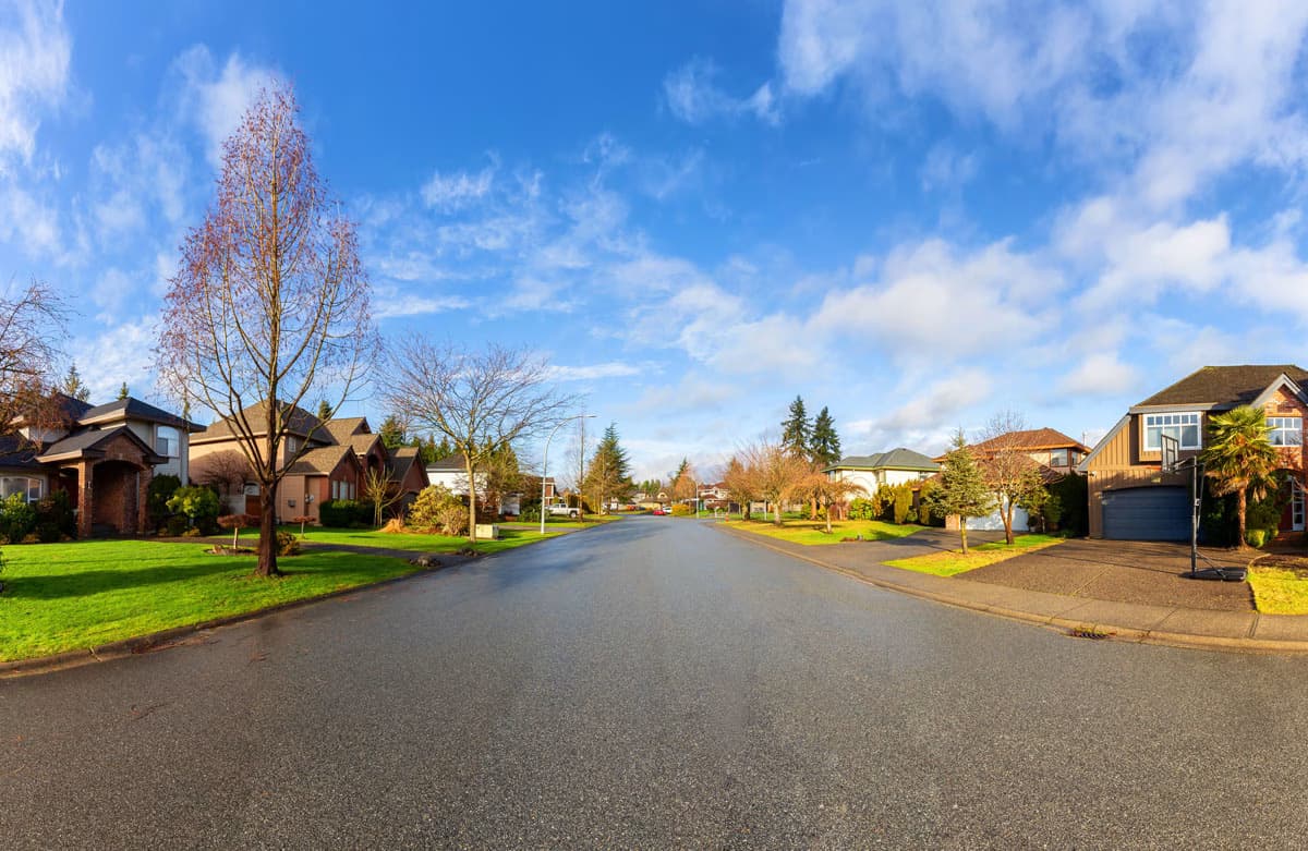 Quiet residential street in a suburban neighborhood in Surrey, British Columbia, with houses and trees under a blue sky.