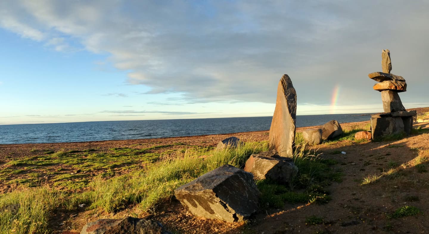 View of Hudson Bay from Churchill, Manitoba, with Inukshuk sculptures and a rainbow in the distance.