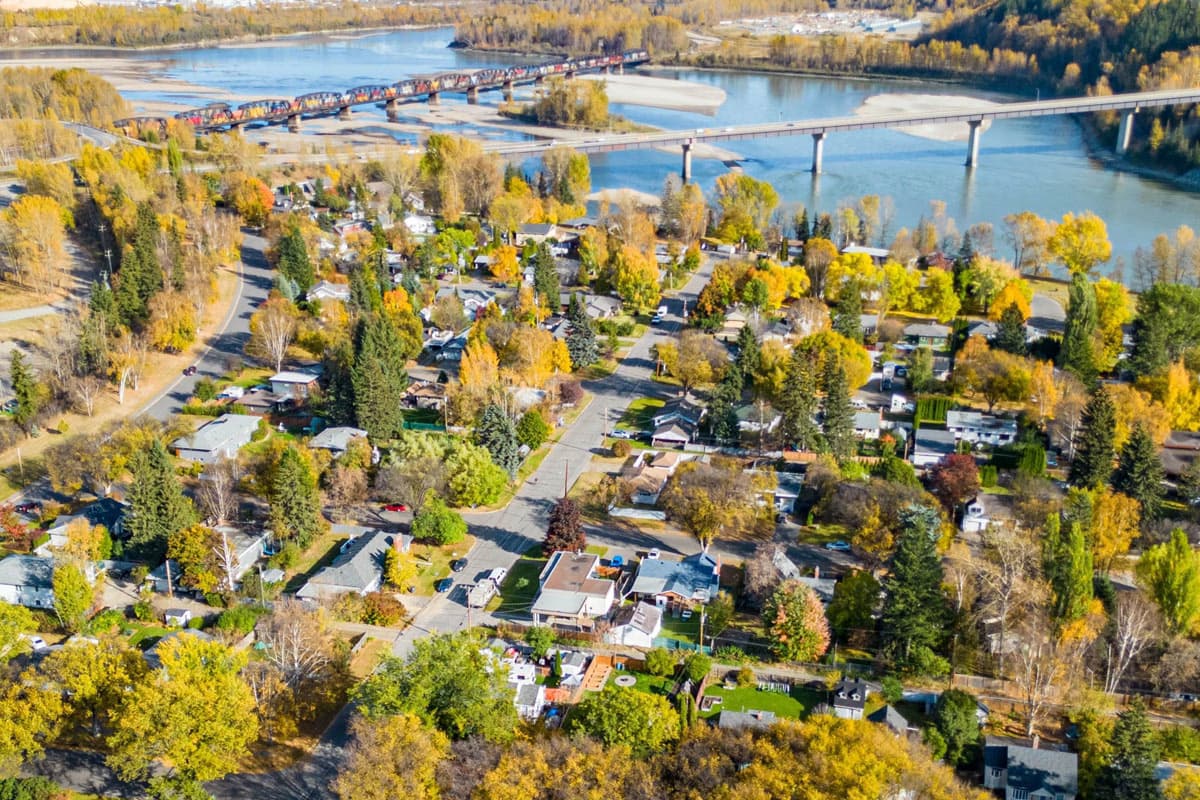 Aerial view of a neighbourhood in Prince George, with a river and a bridge in the background surrounded by autumn foliage.