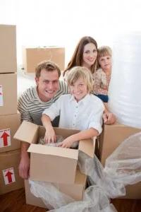 Family smiling while unpacking moving boxes in their new home.