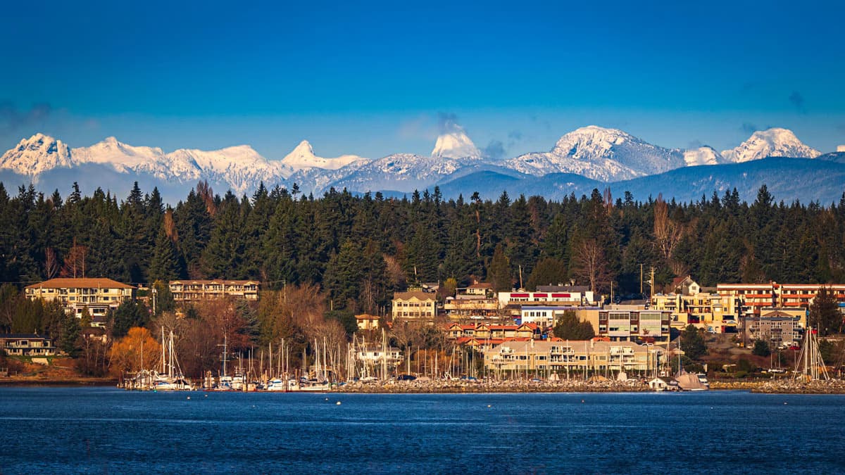 Scenic view of Comox, a coastal town with boats, surrounded by trees, with snow-capped mountains in the background.