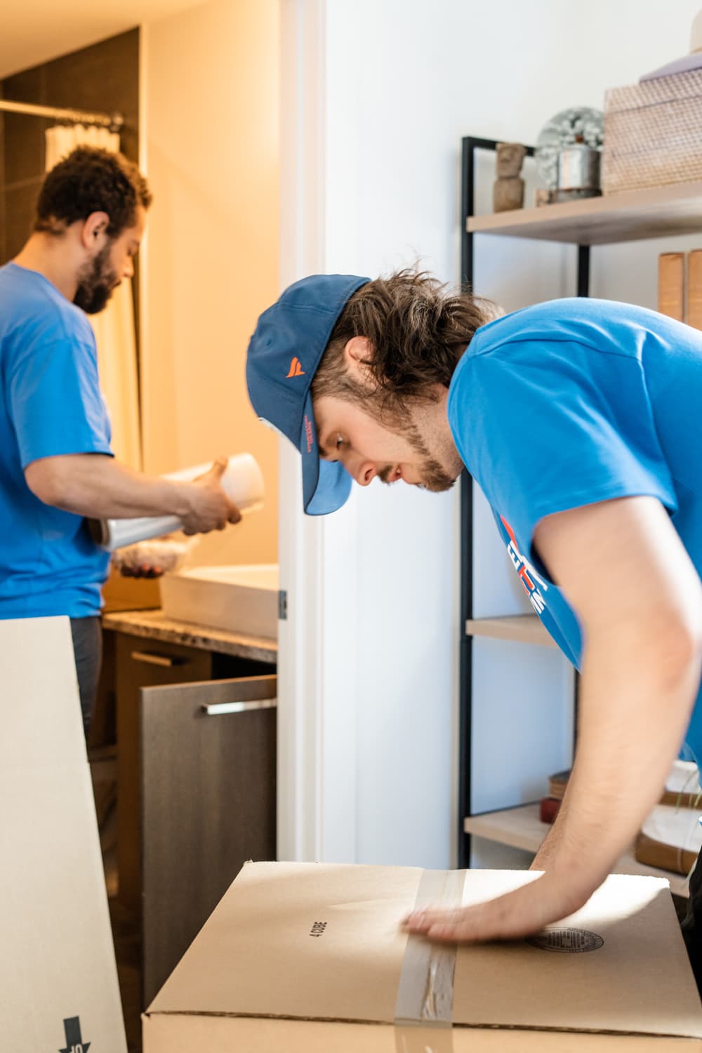 Two movers packing and taping boxes in a home