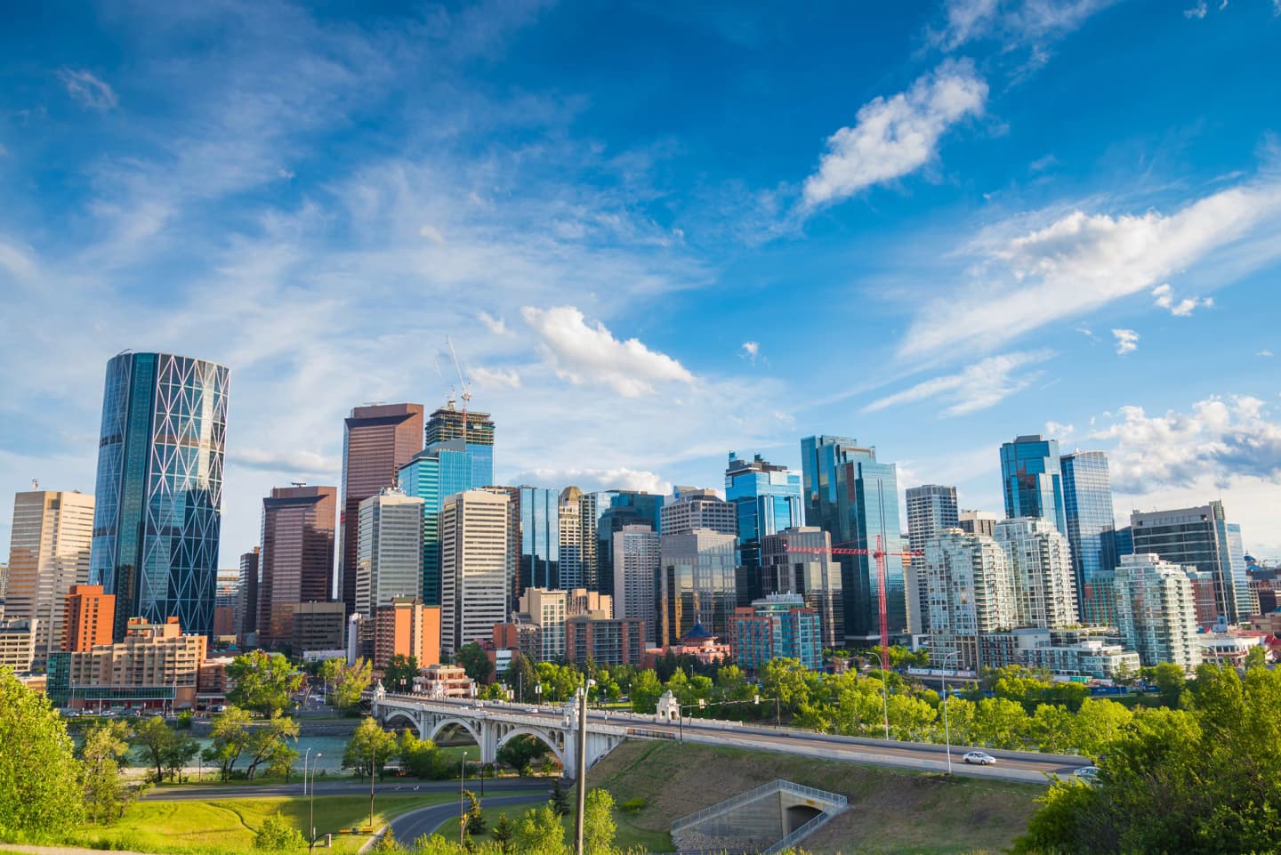 Cityscape of Calgary with modern skyscrapers and a bridge in the foreground on a clear day.