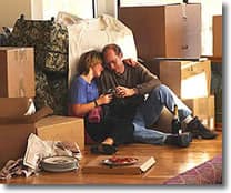 Couple sitting on the floor surrounded by moving boxes, sharing a moment during unpacking