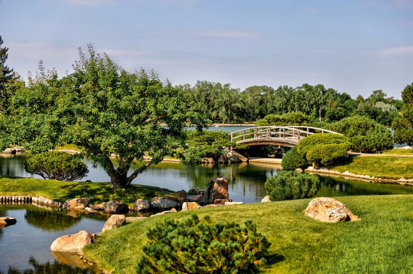 Scenic garden in Lethbridge featuring a wooden bridge over a pond surrounded by lush greenery.