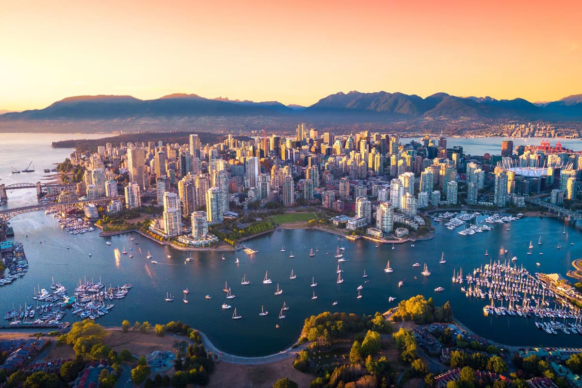 Aerial view of downtown Vancouver, British Columbia, at sunset with boats in the harbor and mountains in the background.