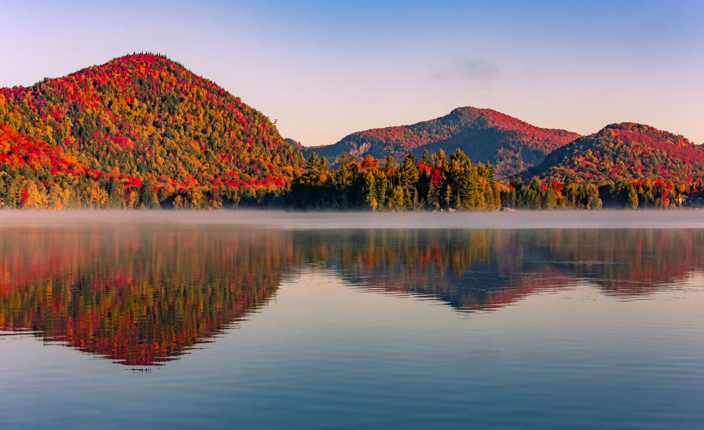 Autumn foliage reflecting on the calm waters of a lake in the Laurentian Mountains, Quebec, at sunrise.