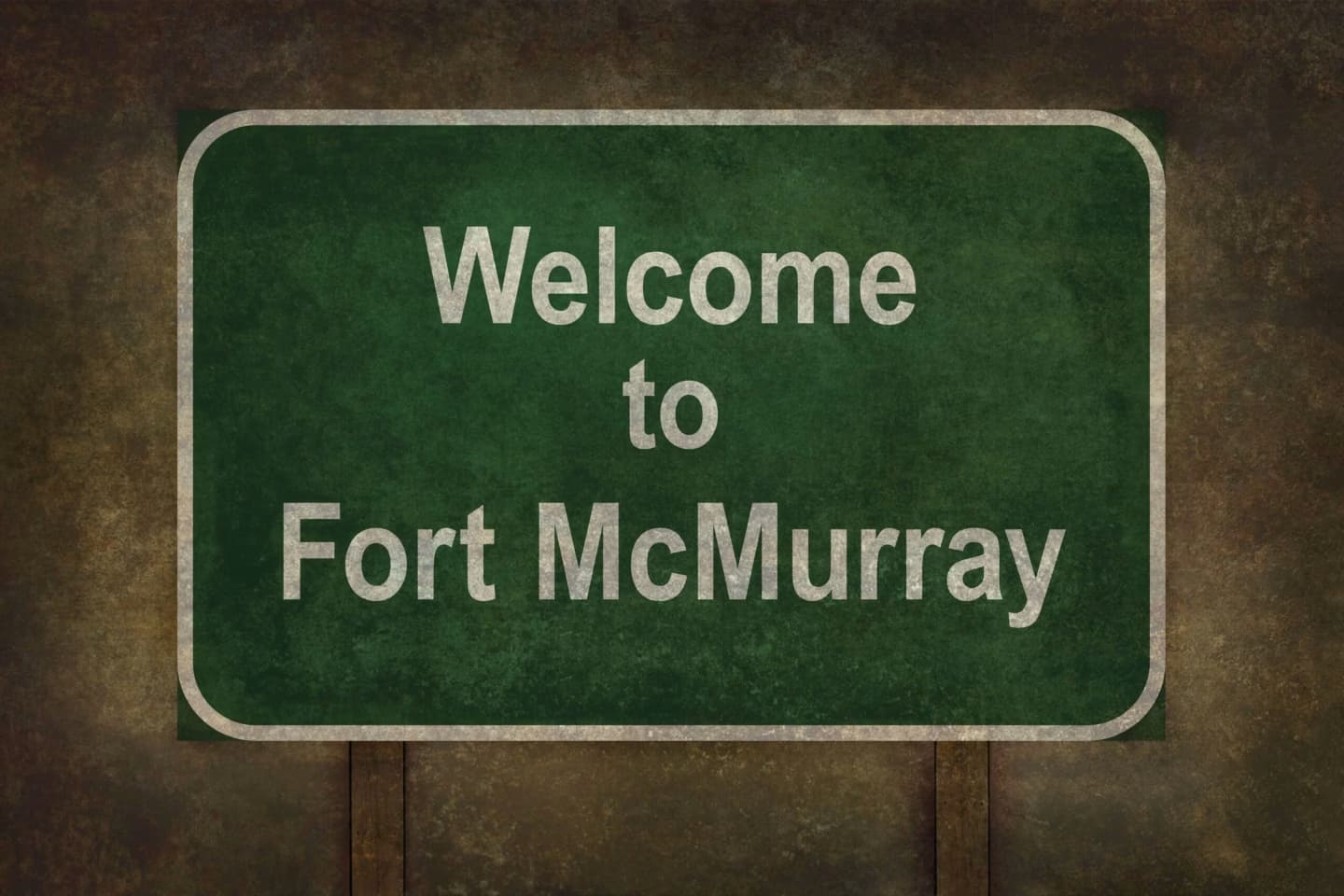 Welcome to Fort McMurray sign, featuring white text on a green background, with a weathered appearance.