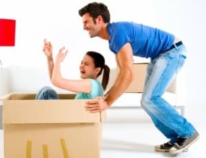 Man playfully pushing a woman sitting inside a cardboard box, both laughing.