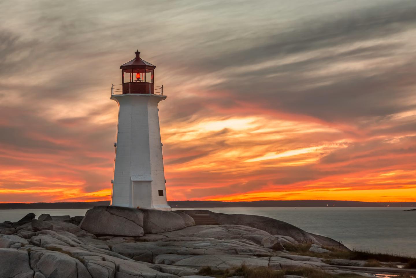 Peggy's Cove Lighthouse in Nova Scotia at sunset with dramatic sky.