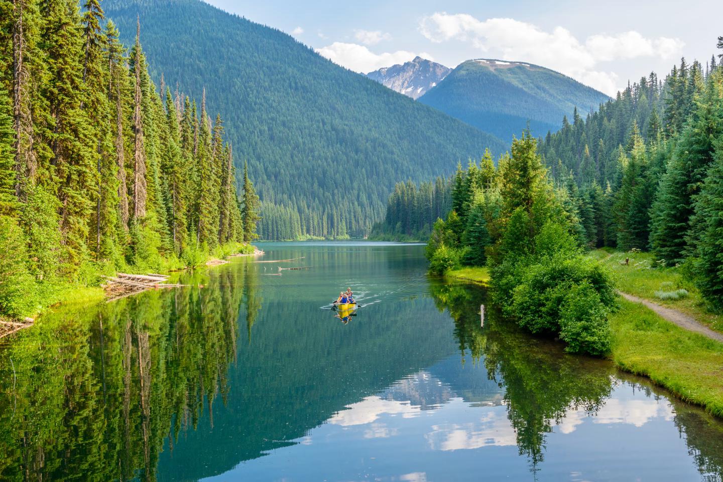 Kayakers on a peaceful lake surrounded by forest and mountains in British Columbia