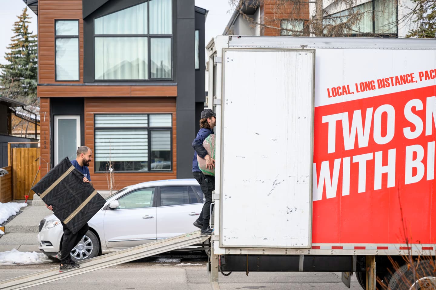 Movers from Two Small Men with Big Hearts Moving loading furniture into a truck in front of a modern house.