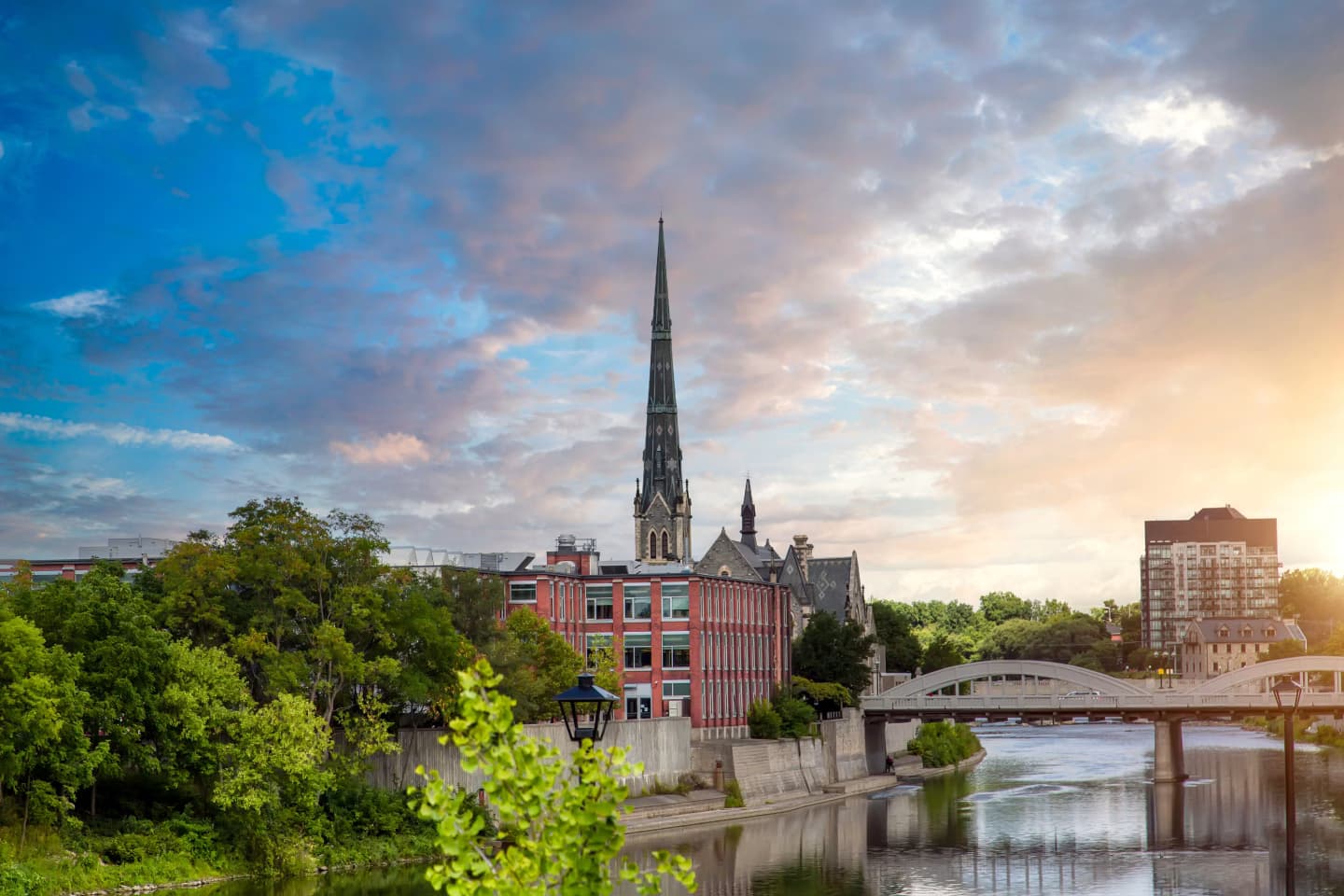 Scenic view of downtown Cambridge, Ontario, featuring a historic church and the Grand River at sunset.