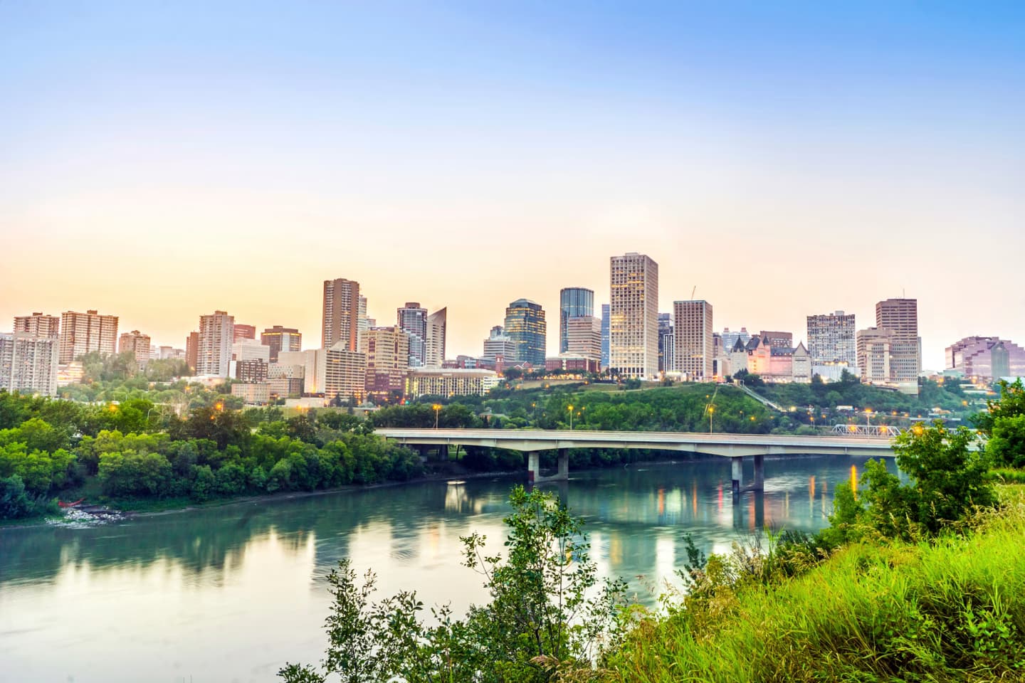 Edmonton city skyline at sunrise with the river and bridge in the foreground.