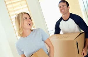 Smiling couple carrying moving boxes into a new home.